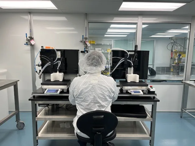 Gowned operator working two benchtop small-fill stations inside a cleanroom